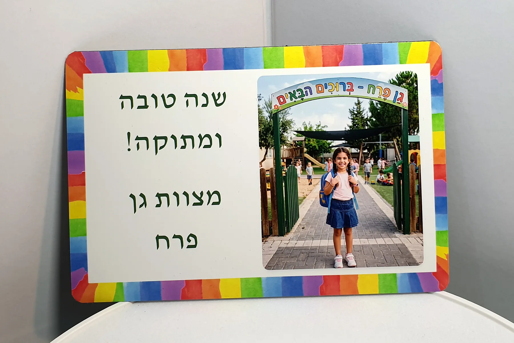 מגנט עם ברכת שנה טובה ותמונת ילדה בכניסה לגן, במסגרת צבעונית